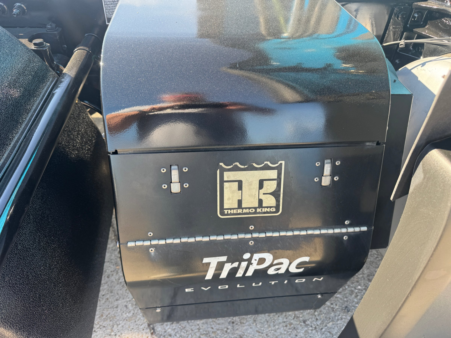 Peterbilt 579 engine bay area with Thermo King TriPac Evolution auxiliary unit mounted under hood and visible tubing; black exterior panels with TriPac Evolution badge.