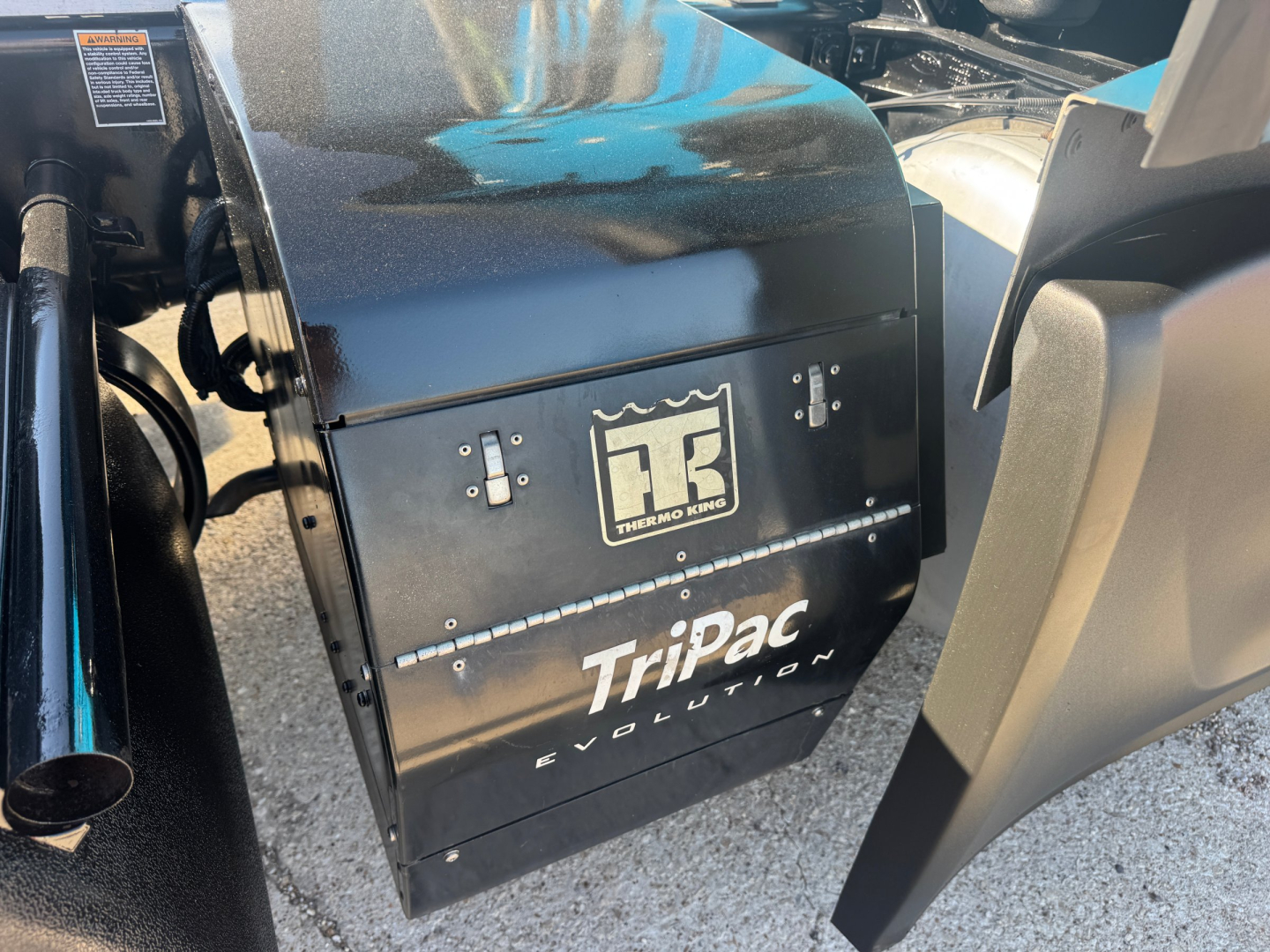 Peterbilt 579 engine bay area showing TriPac Evolution auxiliary heater/AC unit by Thermo King with black metal enclosure and 'TriPac Evolution' text.