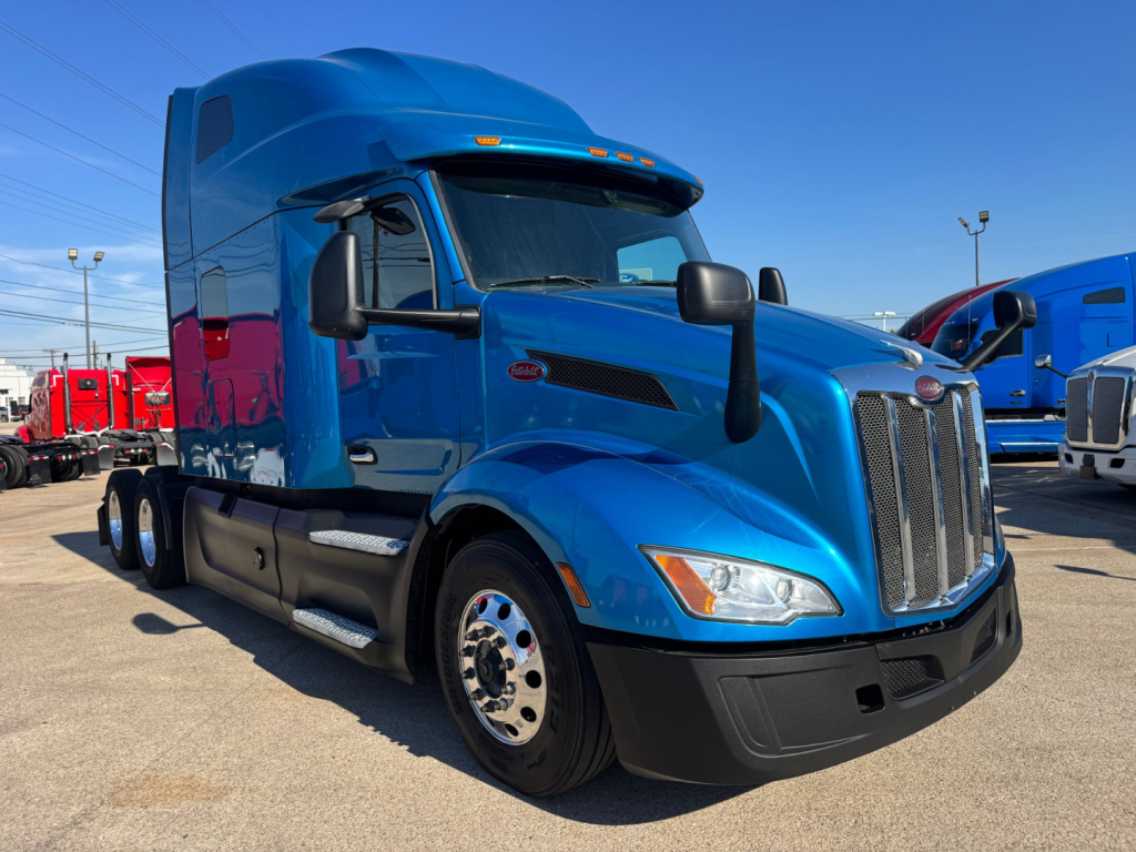 Peterbilt 579 truck in blue, side view, sleeper cab, chrome grille, daytime running lights, black bumper, fuel tanks, multiple rear axles.