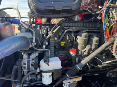 Peterbilt 579 engine bay with visible coolant reservoir, hoses, and various components in front engine area.