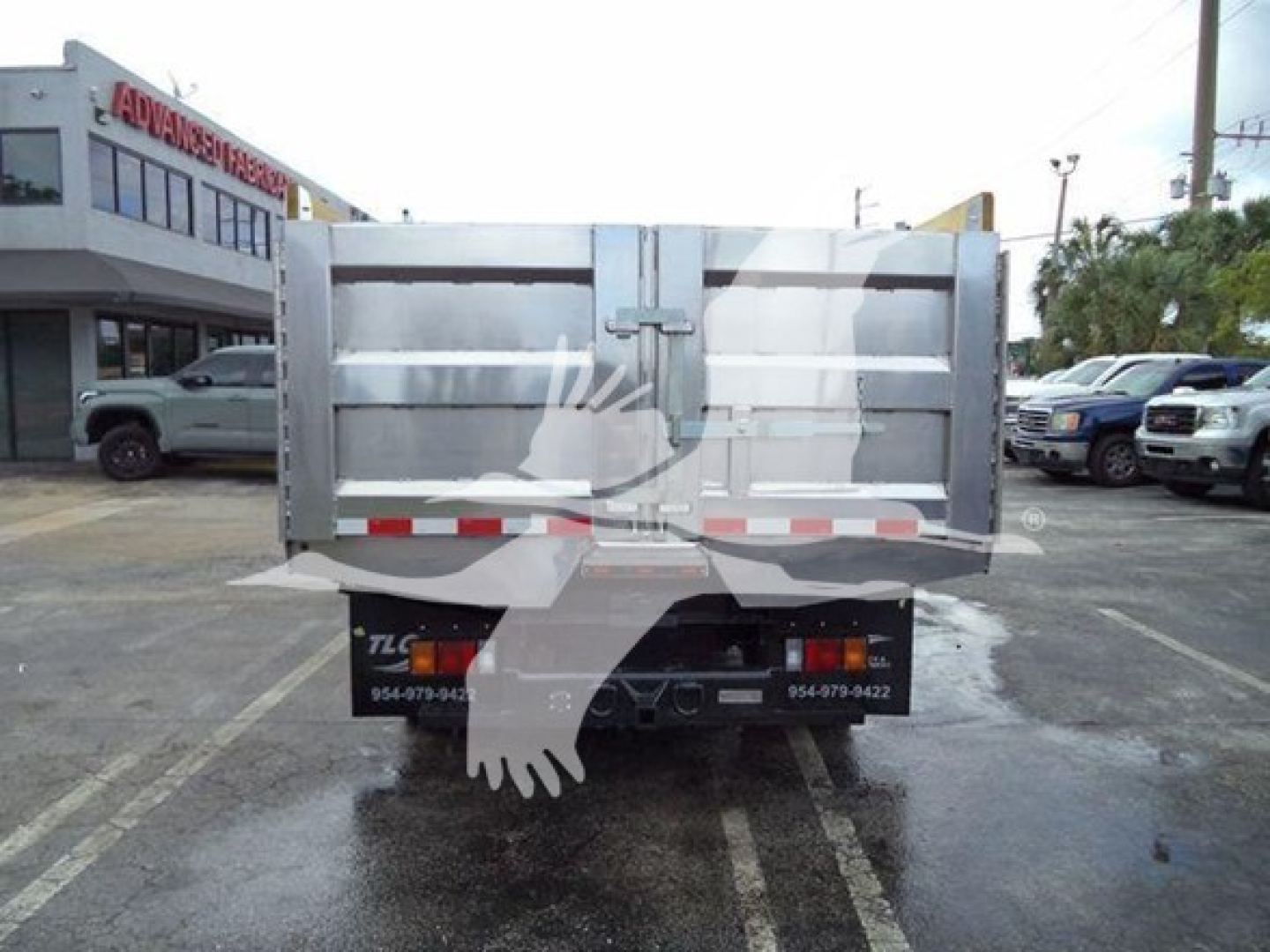 Isuzu NPR/XX dump truck bed rear view showing metal tailgate, reflective tape, and bumper with contact text.