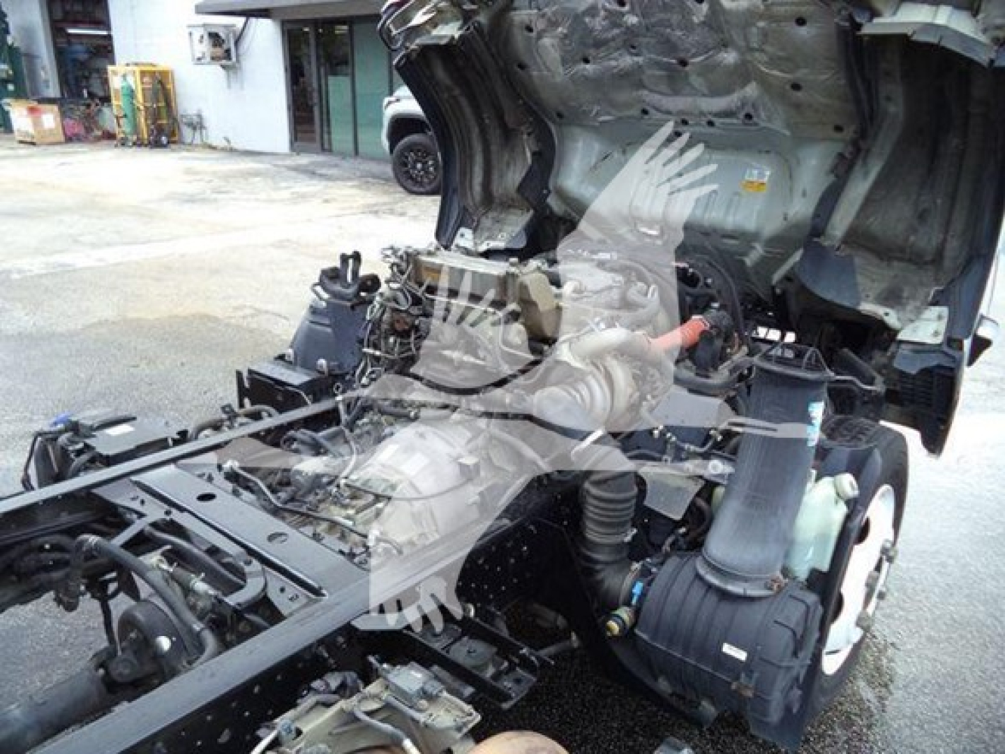 Isuzu NPR XD truck chassis with exposed engine and drivetrain components under a lifted cab; view shows frame, air intake, hoses, and partial cab structure.