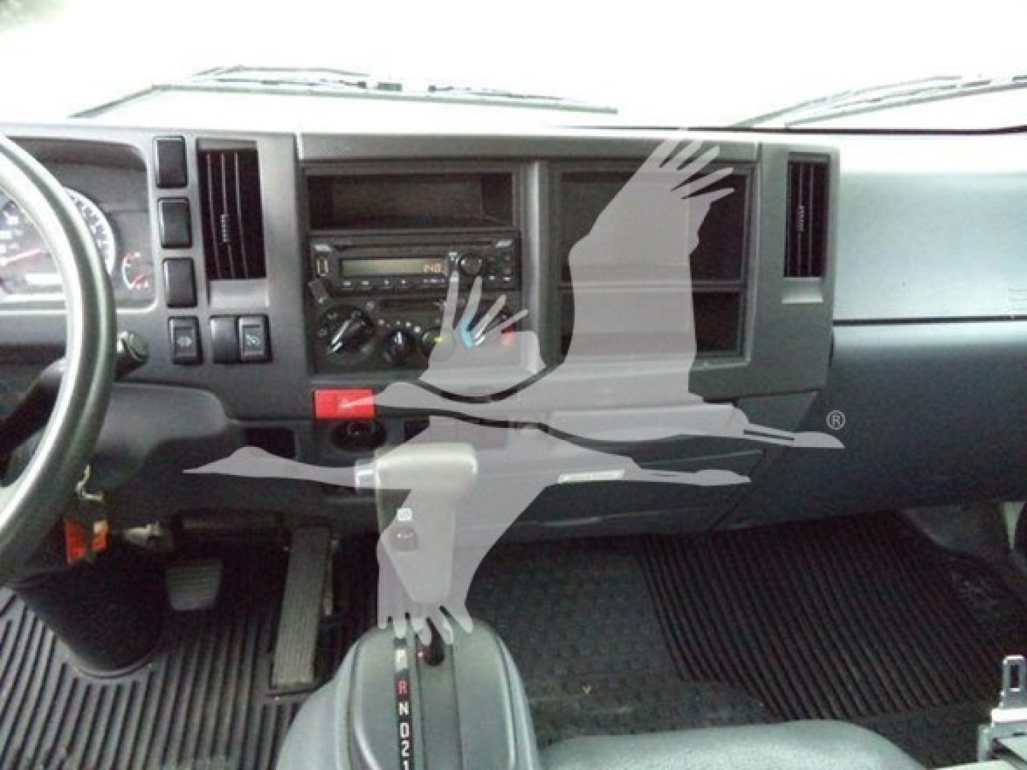 Dashboard view of a 2020 Isuzu NPRXD truck interior showing steering wheel, center stack, gear selector, and floor mats.