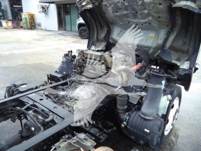 Isuzu NPR XD truck chassis with exposed engine and drivetrain components under a lifted cab; view shows frame, air intake, hoses, and partial cab structure.