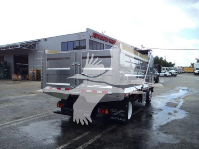 Isuzu NPR XD dump truck rear view showing dump bed and taillights; dealership background with building and lot.