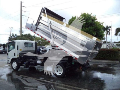 Isuzu NPR XD dump truck with tilted silver dump bed, hydraulic lifting mechanism visible, white cab, wet pavement.