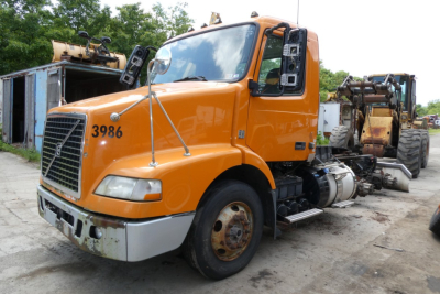 Volvo VNM64T conventional daycab truck showing front grille and orange cab with stock number 0612232 and 3986 on hood.