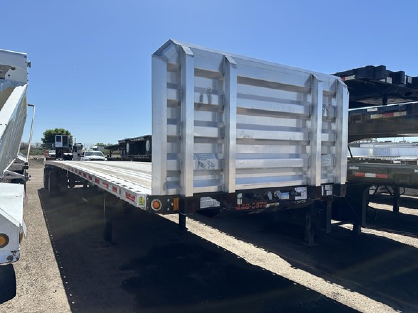 Flatbed trailer with a large rear spread air combo gate, aluminum side rails, and rear gate in a raised position. Visible on the back: reflective markings, taillights, and support legs.
