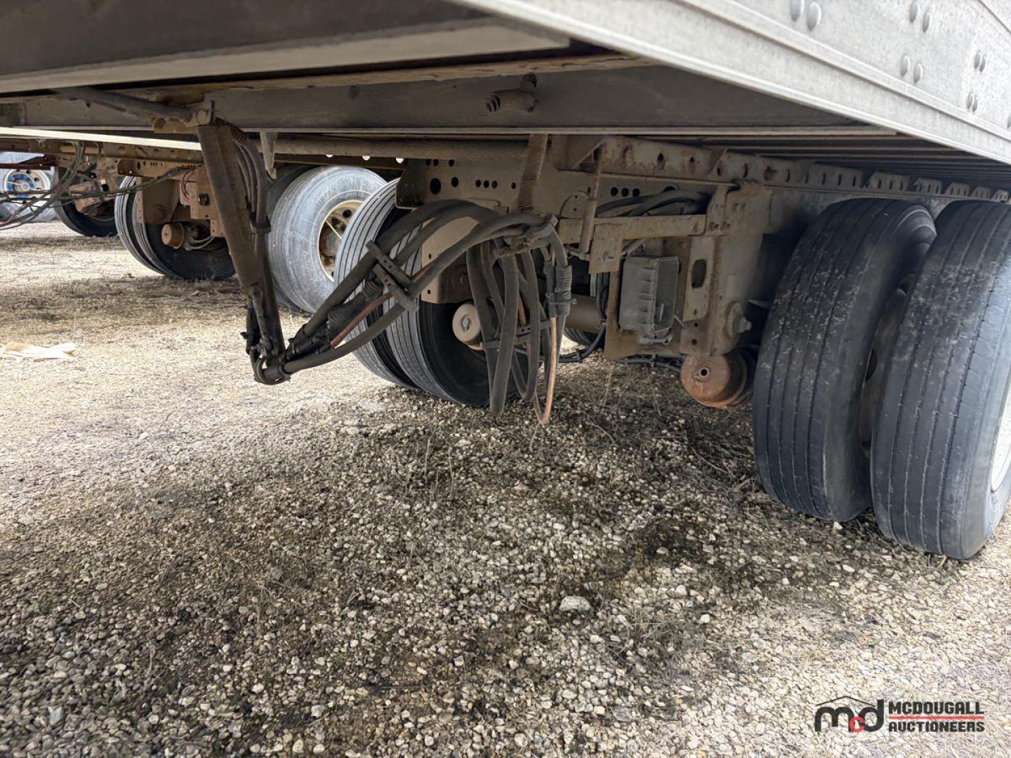 Trailer undercarriage showing dual rear axles and air lines with suspension and wheel hubs visible.