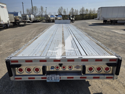 Trailer rear view of a 2019 Reitnouer Dropmiser flatbed trailer, long aluminum deck, multiple taillights, and a centered spare wheel hub area. License plate visible.