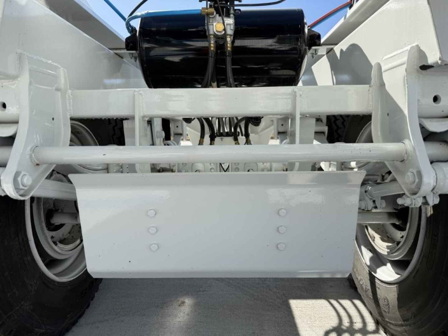 Trailer hitch area showing undercarriage with white metal frame, axles, suspension, and a rectangular skid plate/dodge shield with bolts.