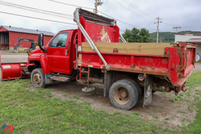 Truck bed with dump body showing red GMC TopKick C5500 with plow and wooden stake bed side panels.