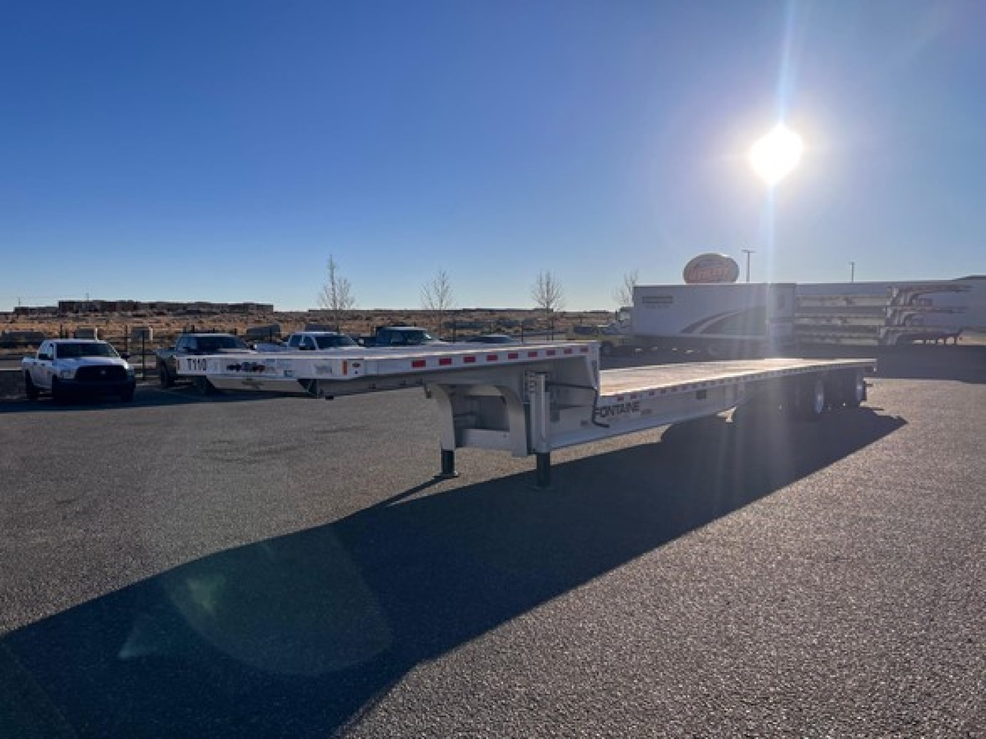 Fontaine Revolution drop deck trailer in a parking lot showing long flatbed with dual axles and support legs.