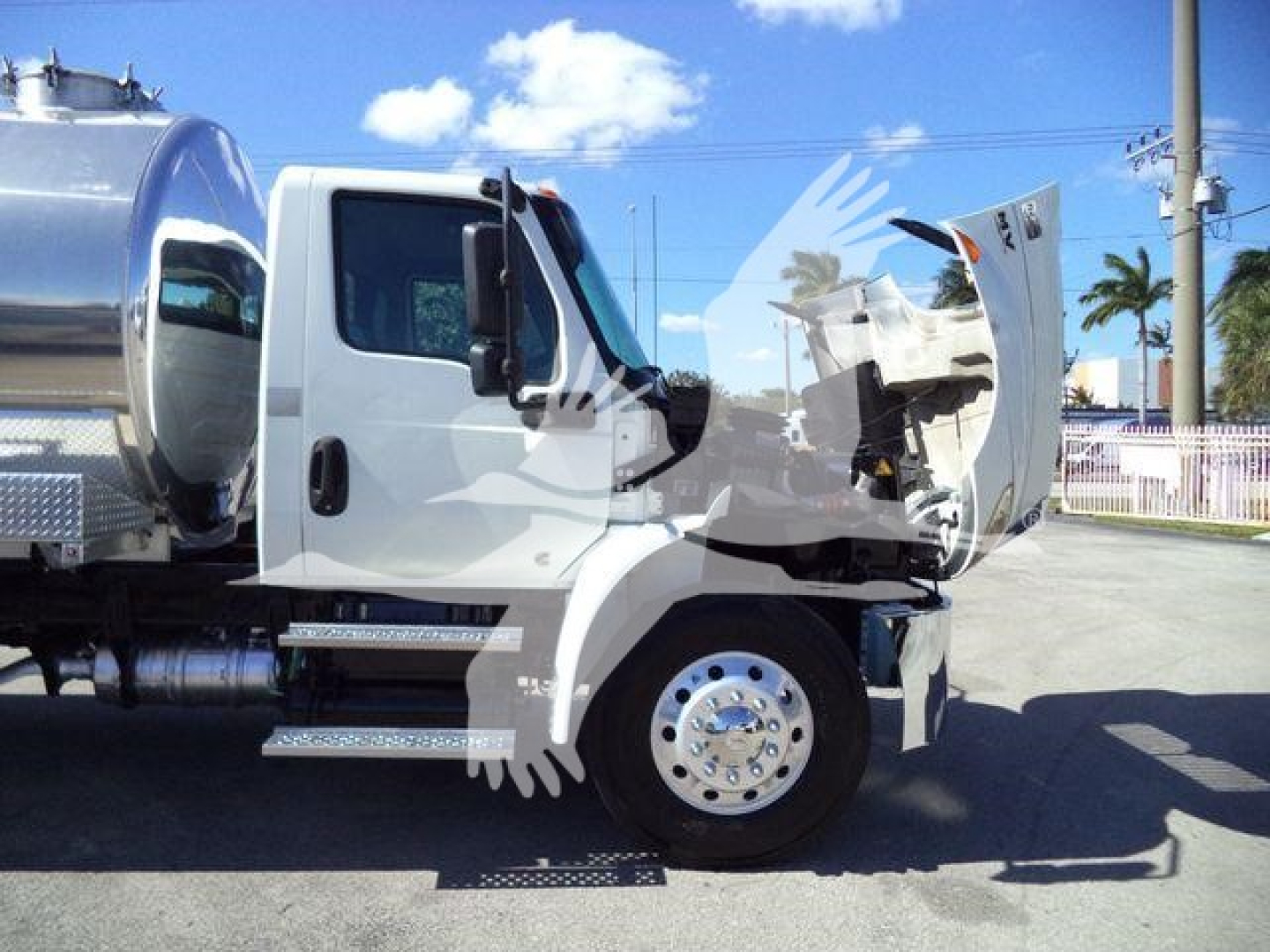 Tractor truck cab and vacuum tank side view showing front wheel and open hood on a white International MV truck.