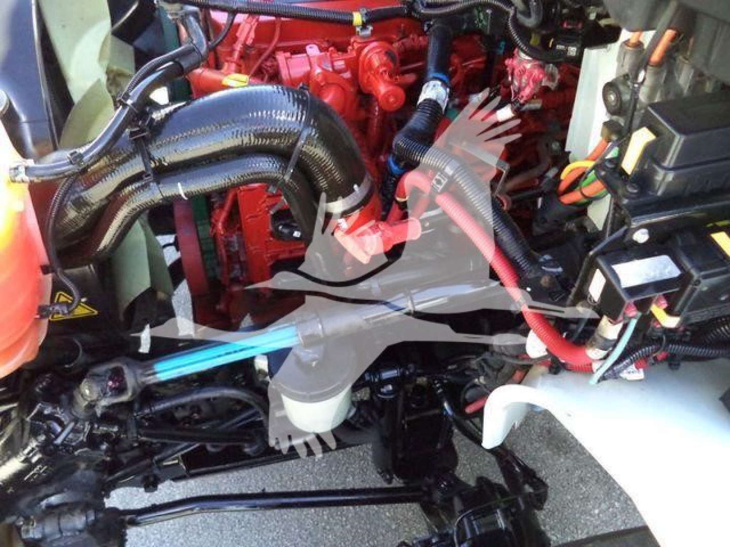 Engine bay of a 2021 International MV vacuum tanker showing red engine components, black hoses, wiring, and a white reservoir; view focuses on mid-section of the engine bay.