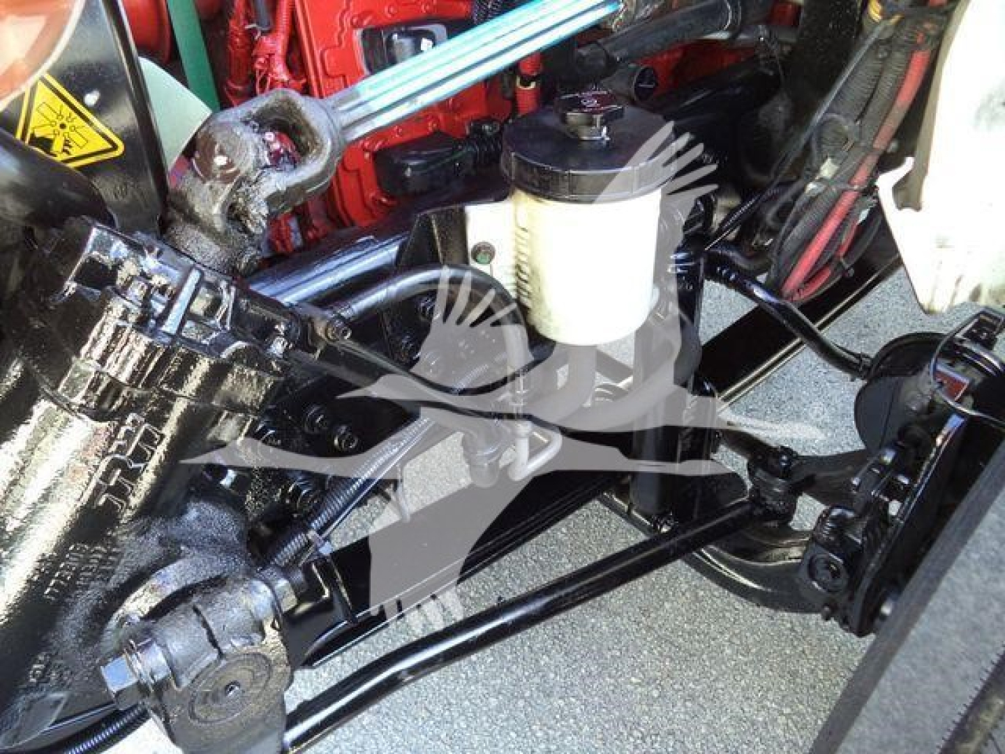 Suspension and hydraulic lines in a vacuum tank truck engine bay with brake master cylinder and connected hoses.