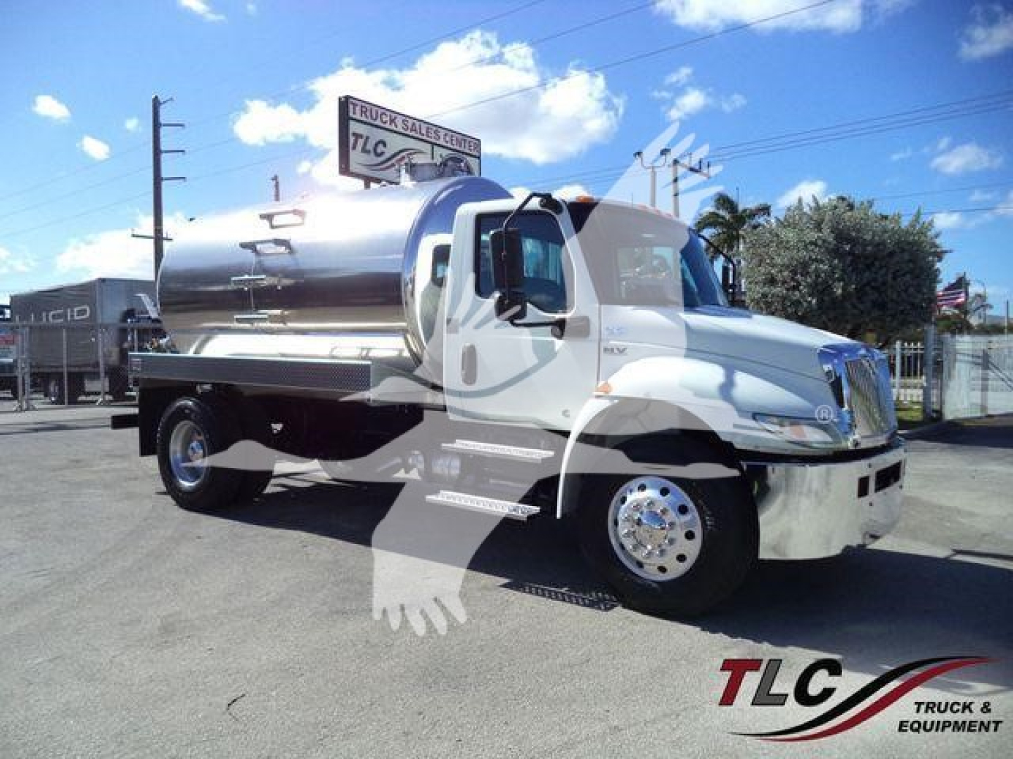 International MV vacuum tank truck with polished steel tank and white cab, side view, dealership lot in background.