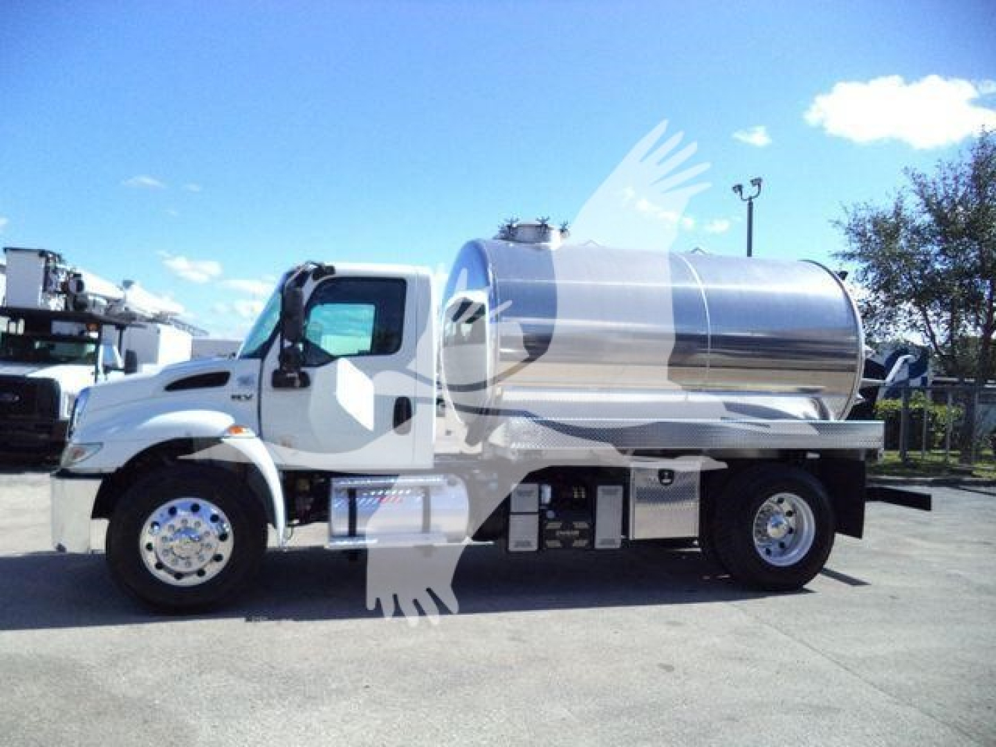 Vacuum tank truck, white International MV, side view showing polished stainless steel tank with rounded ends, dual rear wheels, chrome accents, and access panels.