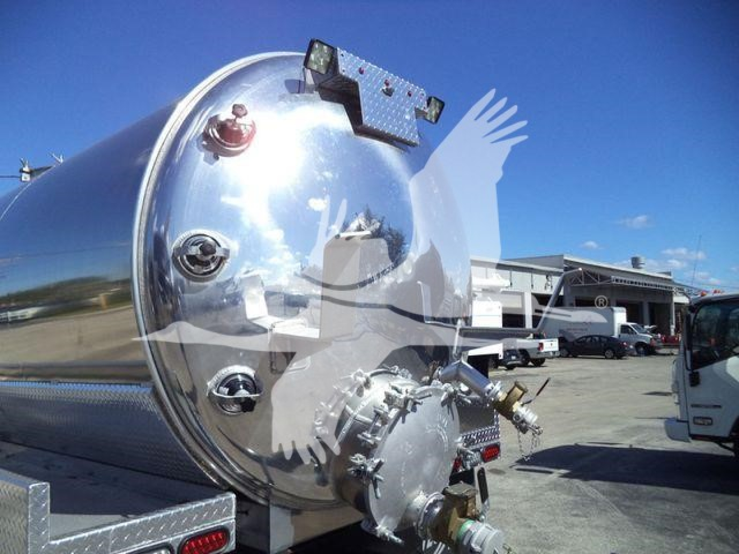 Large polished cylindrical vacuum tank trailer or storage tank with manhole and fittings, mounted on a wheeled trailer frame. Industrial setting visible in background.