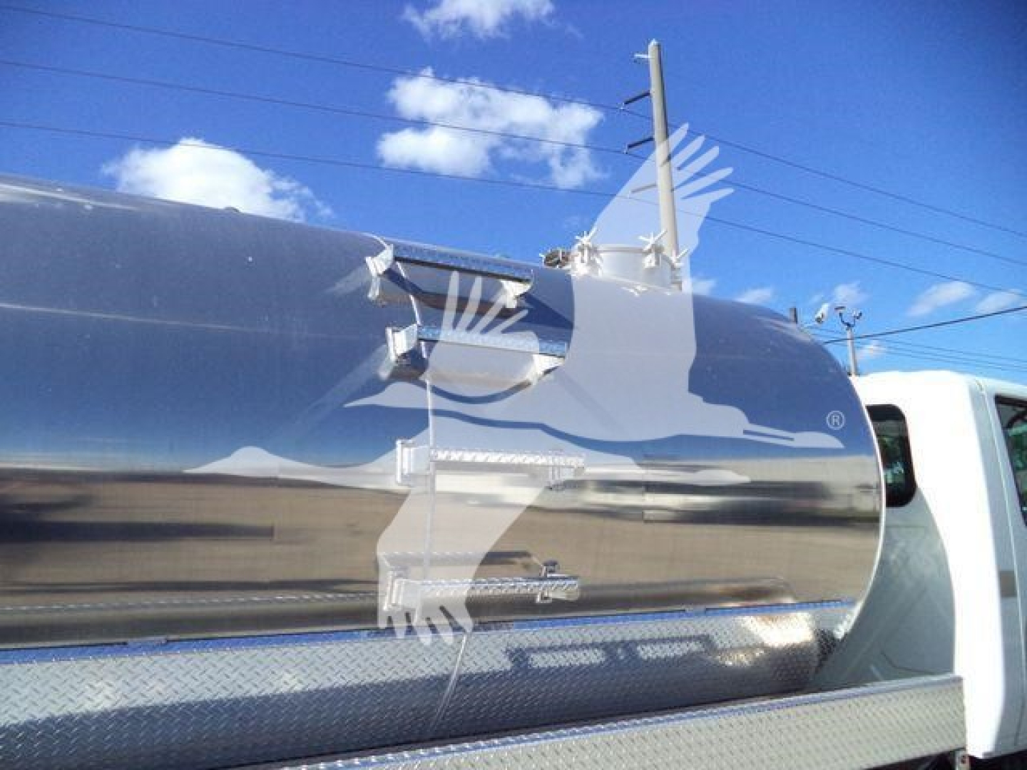 Front-right quarter of a 2021 International MV vacuum tank truck showing a polished stainless steel cylindrical tank with access hatch, ladder and diamond-plate step.