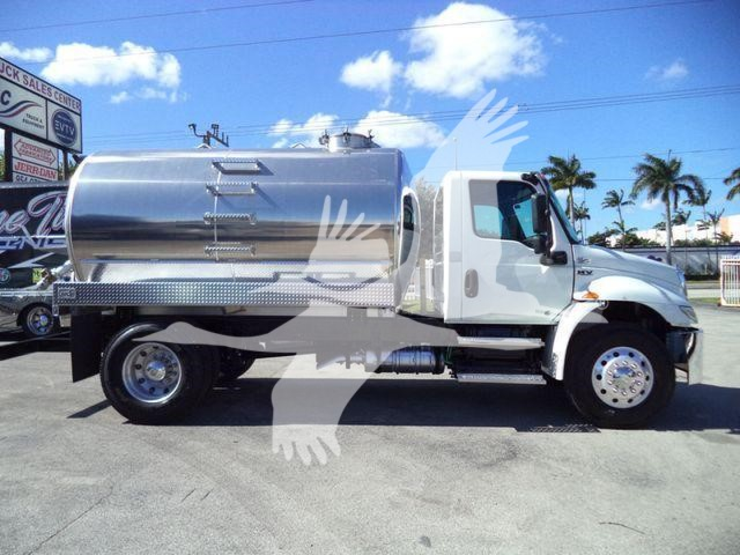 Side view of a white 2021 International MV vacuum tank truck with shiny stainless steel cylindrical tank, chrome front bumper, dual rear wheels, and palm trees in background.