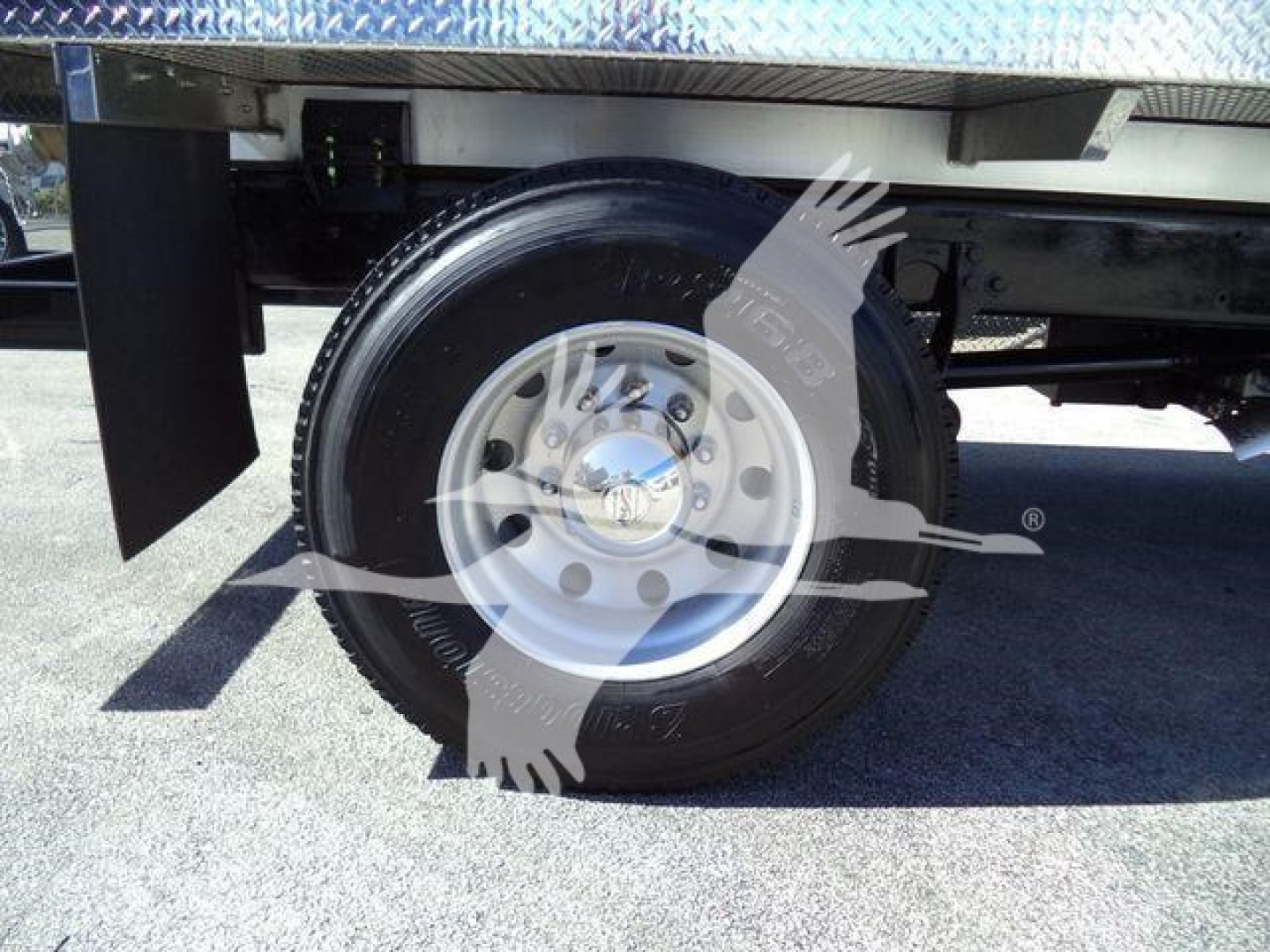Wheel and tire assembly of a vacuum tank truck with visible rim and hub, undercarriage components and frame in the background.