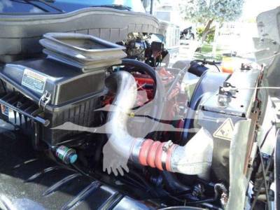 Truck engine bay showing vacuum tank with large air intake, hoses, and warning label.