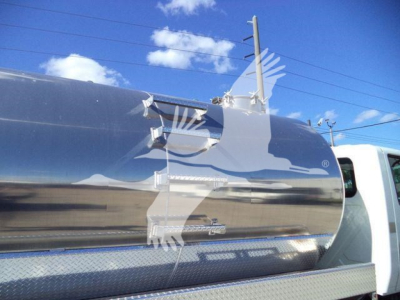 Front-right quarter of a 2021 International MV vacuum tank truck showing a polished stainless steel cylindrical tank with access hatch, ladder and diamond-plate step.