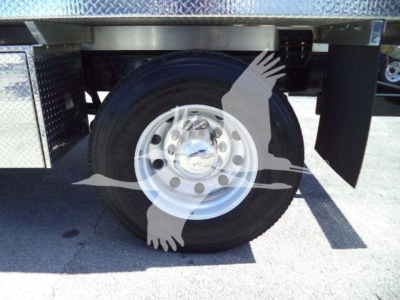 Truck wheel and dual rear axle area showing a steel rim and black tire, undercarriage, with diamond plate toolbox and mud flaps partially visible.