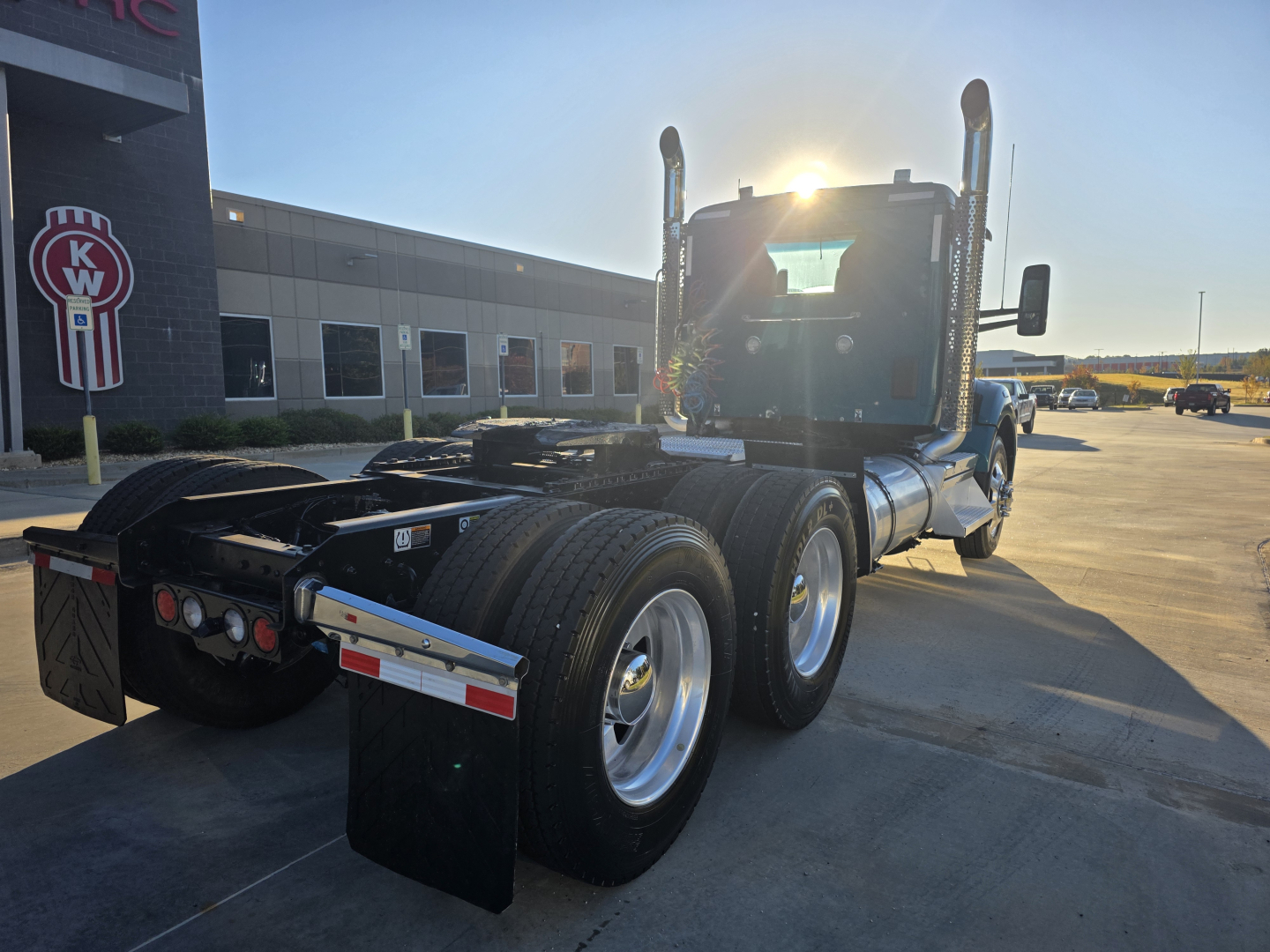 Kenworth T880 conventional daycab tractor in-service showing rear dual axles and tires, side view, with dealership building in background.