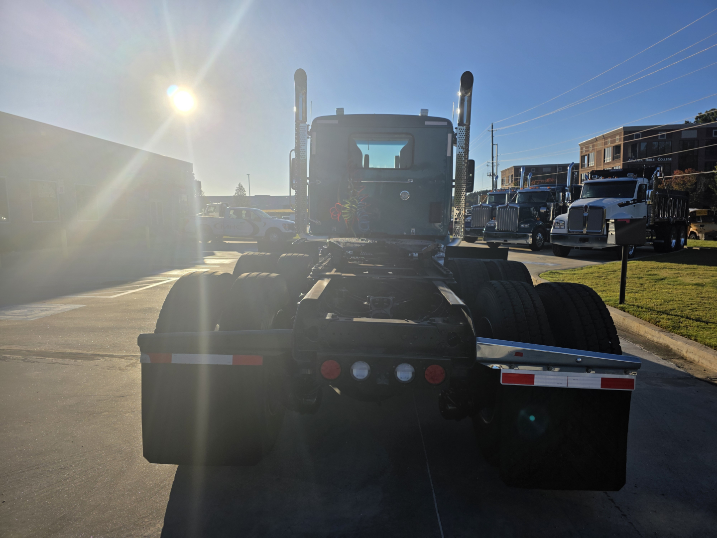 Kenworth T880 rear view showing fifth wheel and dual rear axles under bright sun in a truck lot.