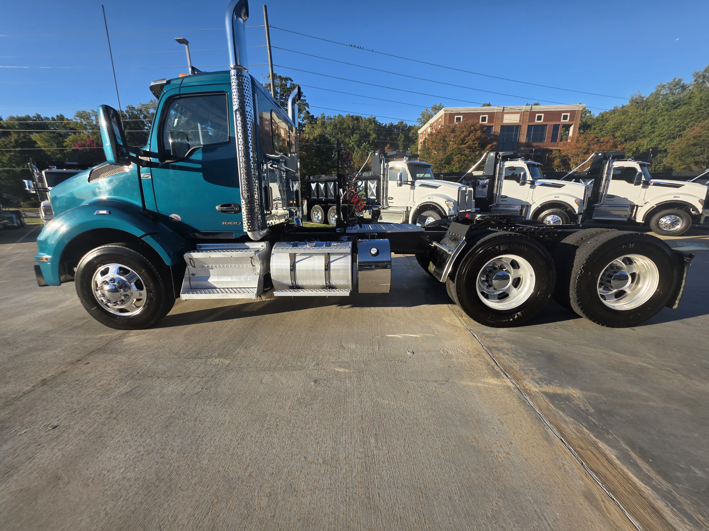 Kenworth T880 daycab truck side view showing teal cab and chrome fuel tanks, dual rear axles, and heavy-duty chassis with chrome exhaust stack.