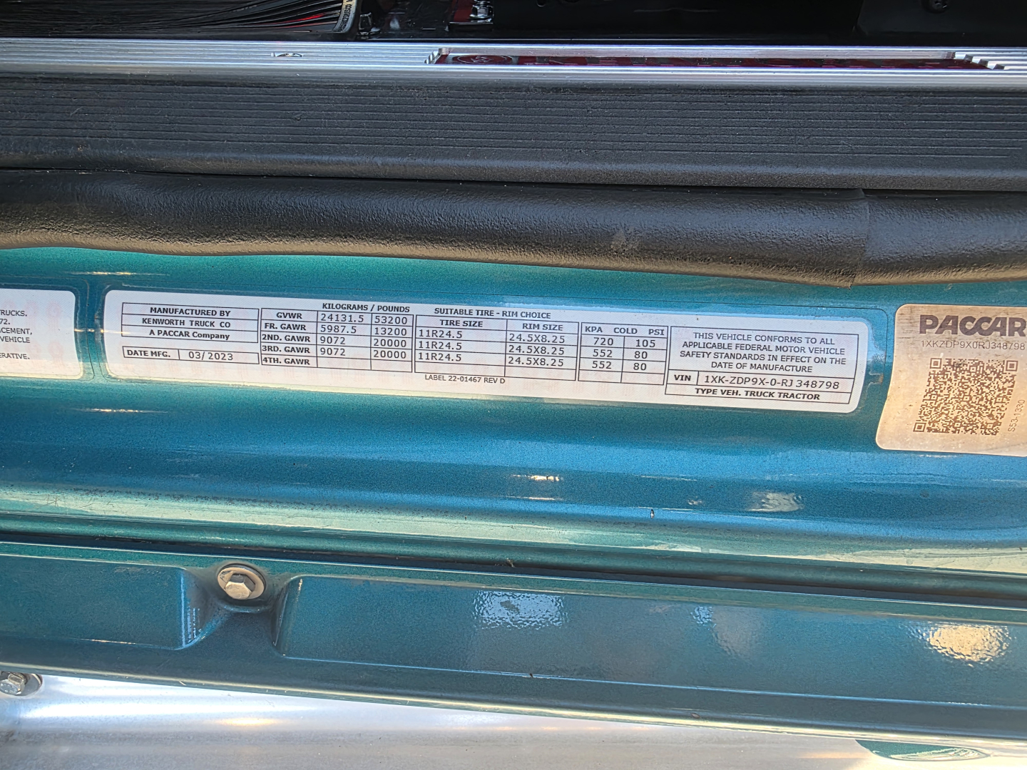 Kenworth T880 engine bay area showing specification label with columns of text and numbers, including manufacturing and tire/weight data; ISO small sticker details visible.