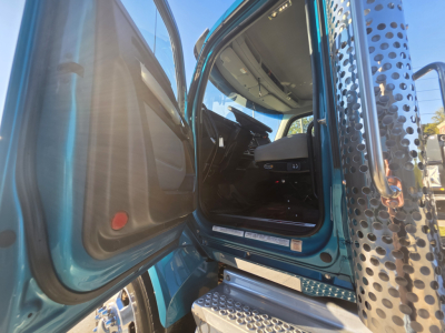Kenworth T880 cab interior entry with open door showing driver seat and dashboard, blue exterior, perforated exhaust stack visible.