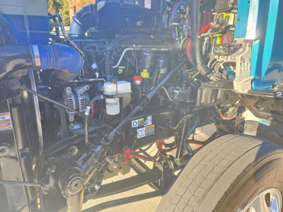 Kenworth T880 engine bay showing fuel filter, various hoses, wiring, and front wheel in view.