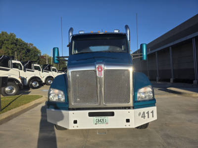 Kenworth T880 conventional daycab front view showing large chrome grille, teal fenders, white bumper, and bumper number 411.