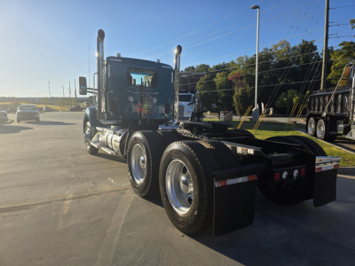 Kenworth T880 conventional daycab tractor side/rear view showing triple rear axle, fuel tanks, exhaust stacks, and fifth wheel kit.
