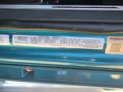 Kenworth T880 engine bay area showing specification label with columns of text and numbers, including manufacturing and tire/weight data; ISO small sticker details visible.