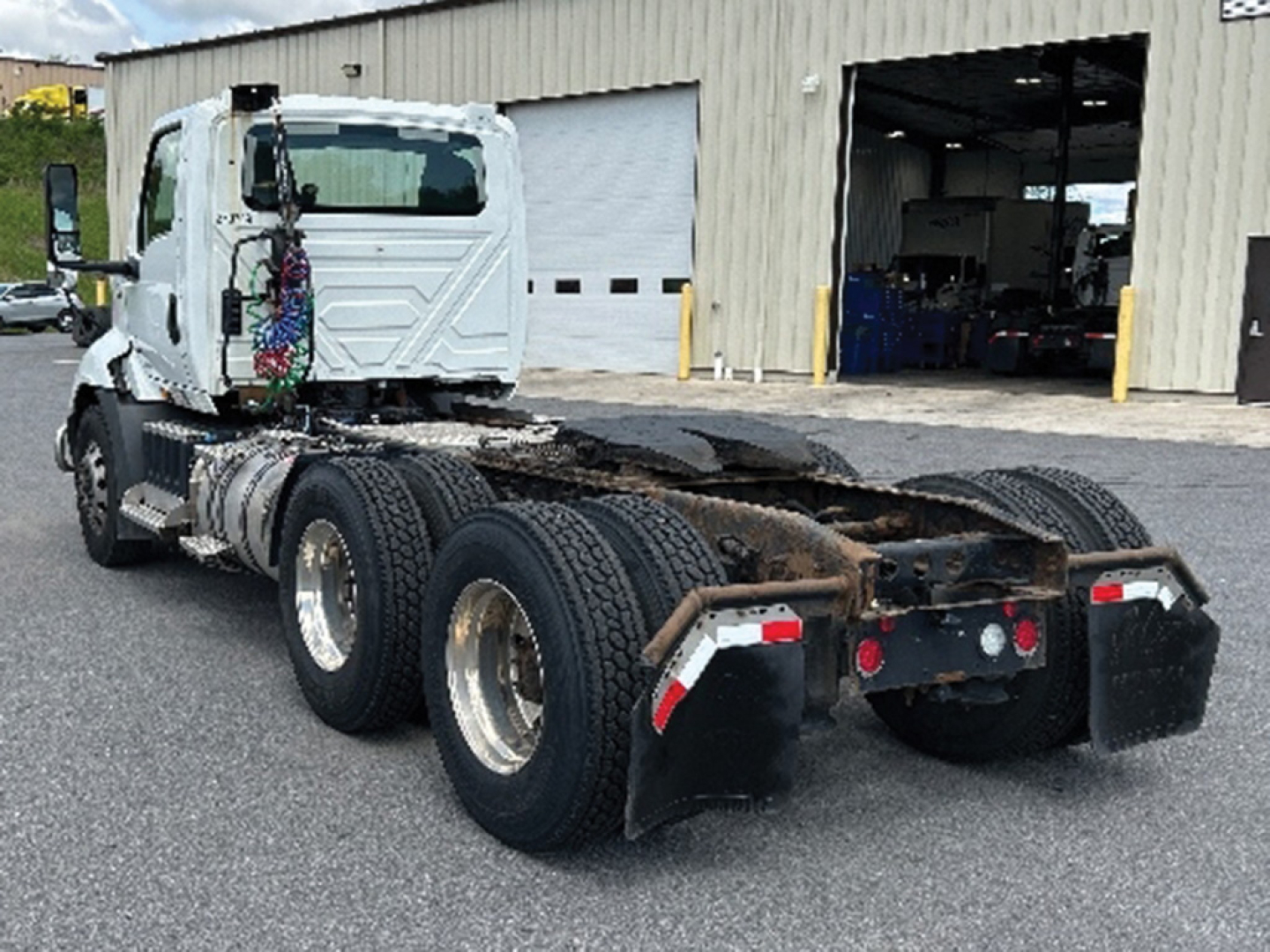 Truck chassis with rear dual-axle configuration and fifth-wheel plate; International RH613 cab facing left, white cab, visible wheel arches, rear mud flaps, in a yard