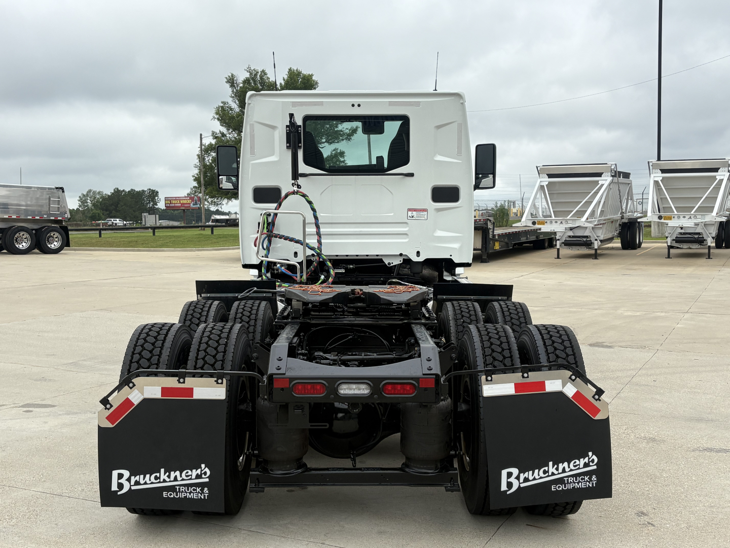 Tractor truck rear view showing dual rear axles, mudflaps with Bruckner logo, and white cab in background.
