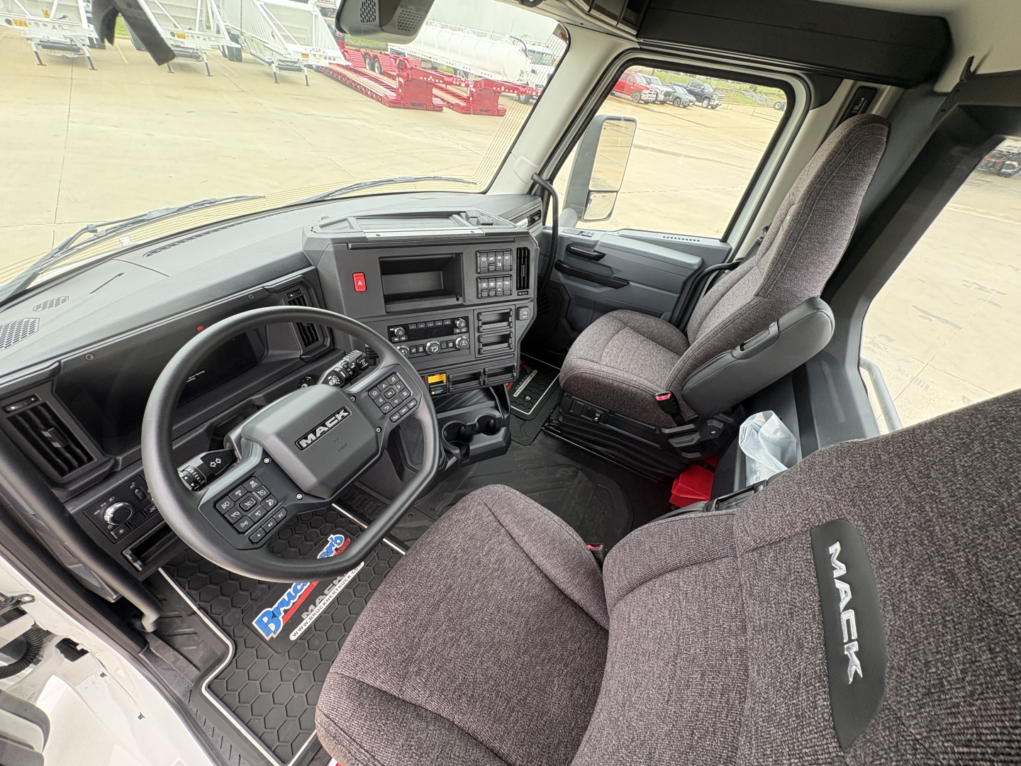 Mack AN64T truck cab interior showing steering wheel with Mack logo, dash controls, center console, and gray fabric seats.