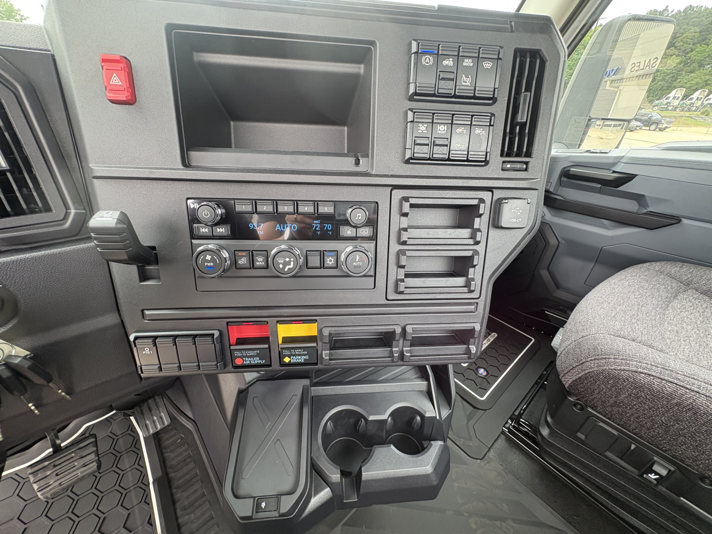 Interior dash of a 2027 Mack AN64T cab showing dashboard controls, climate panel, cup holders, and storage compartments.