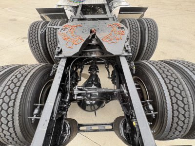 Front view of a Mack AN64T truck chassis showing dual rear axles and drivetrain components, with visible fifth-wheel mount and suspension parts.