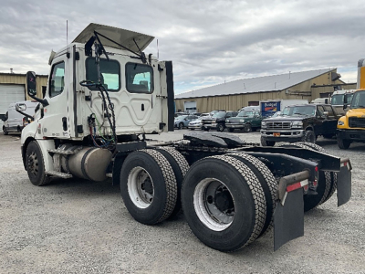 Side view of a 2018 Freightliner Cascadia126 day cab truck chassis with triple rear axles and dual fuel tanks. Visible text on cab includes Freightliner logo and model badge.
