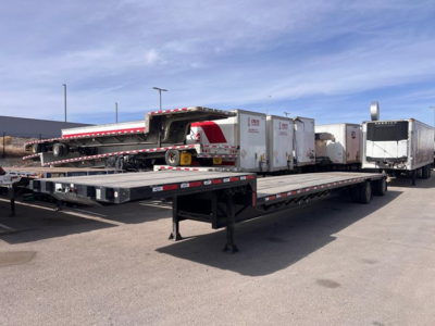 Trailer deck showing long flatbed with loading ramp and three enclosed trailers in background; visible branding on equipment.