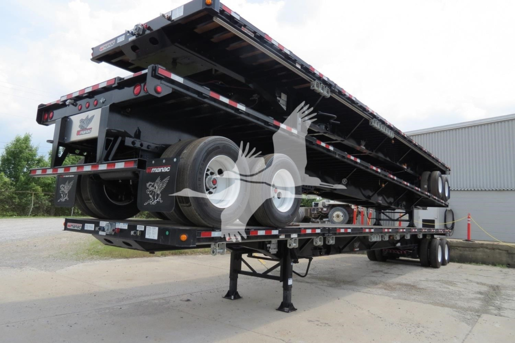 Manac extendable flatbed trailer in stacked position with landing gear down, rear tires, and reflective safety stripes visible.