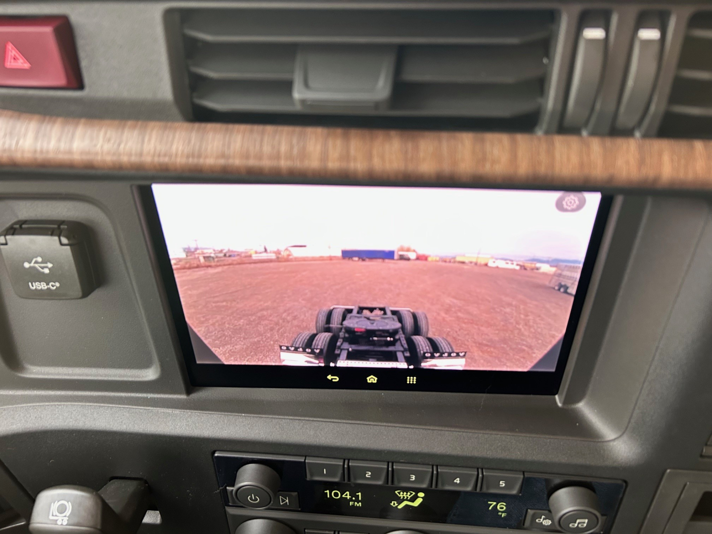 Volvo VNL64T660 dash area with center touchscreen display showing exterior yard view and hitch; dashboard controls and wood trim visible.