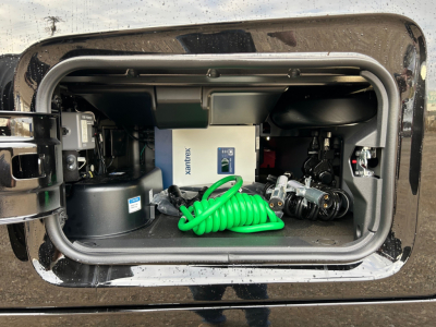 Front storage bay of a Volvo VNL truck showing onboard air compressor unit, green coiled air hose, and various components inside the bay.