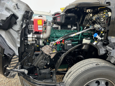 Volvo VNL64T660 engine bay showing green diesel engine, red fire extinguisher, hoses, wiring, and front wheel with tire.