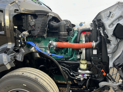 Engine bay of a Volvo VNL64T660 truck showing green engine with red air intake hose, blue hose, black hoses, and fluid reservoirs visible.